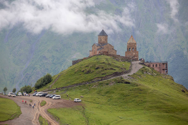 A majestic mountain landscape with a historic church and rolling clouds. Gergeti Trinity Church, under Mount Kazbek near the village of Stepantsminda in Georgia