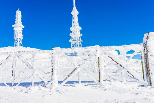 A vibrant winter scene featuring snow-covered communication towers set against a clear blue sky, illustrating the contrast between technology and nature in a frozen landscape.
