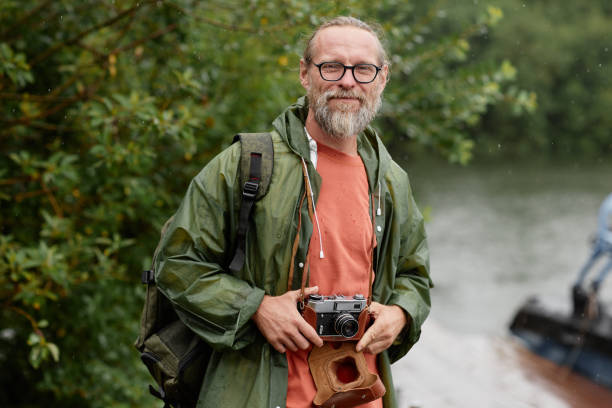 Waist up portrait of smiling male tourist with vintage camera looking at camera while travelling outdoors in nature