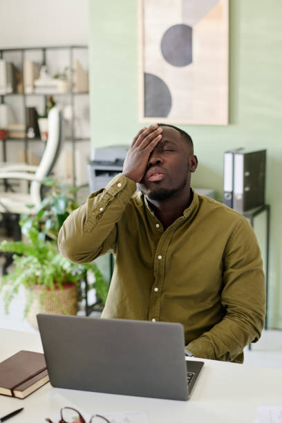 istock African American Man Sitting in Office Holding Head in Hand 2175525327