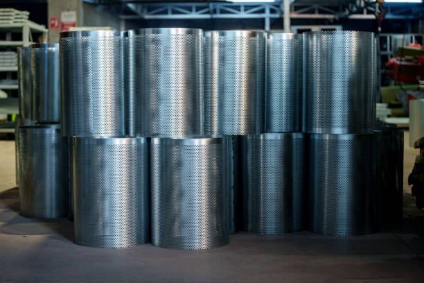 cylindrical filter structures made of metal lined up on a table in a production facility. The filters are made of a fine mesh material, each of the same size and arranged in a symmetrical pattern. The focus is on the top of the filters and the details in the background are blurred, emphasizing the clarity of the products in the foreground. Such filters are often used in industrial filtration processes, cleaning air or liquids.