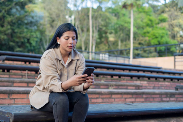 istock Latin woman, smiling while checking her cell phone dressed formally, at noon 2175528187