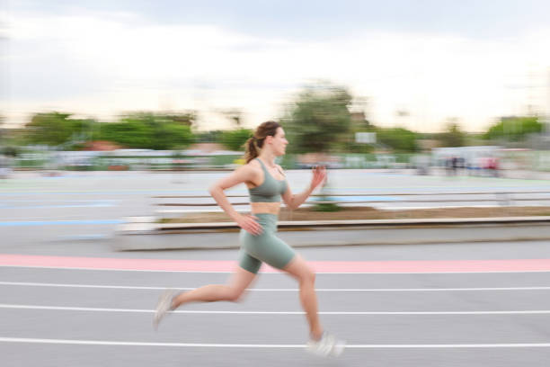 Young sportswoman is running fast on an athletics track with motion blur in an urban environment