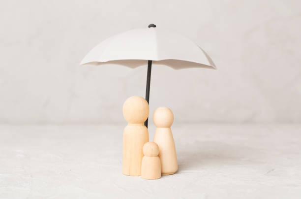 istock Wooden family figures under umbrella on concrete background.Insurance coverage concept. 2175532864
