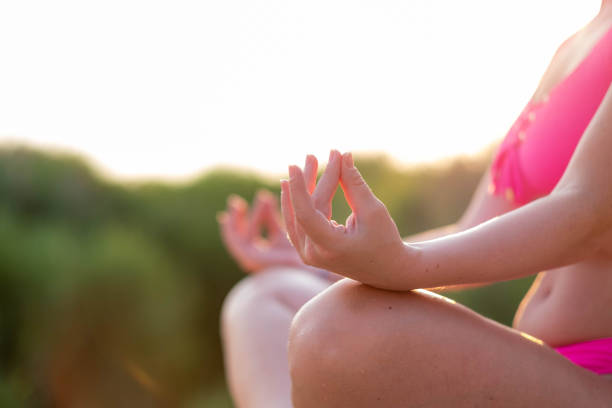 woman on a rock meditating with her legs crossed, with her hands on her legs, in a bathing suit, alone, enjoying nature, next to the water, fingers in focus