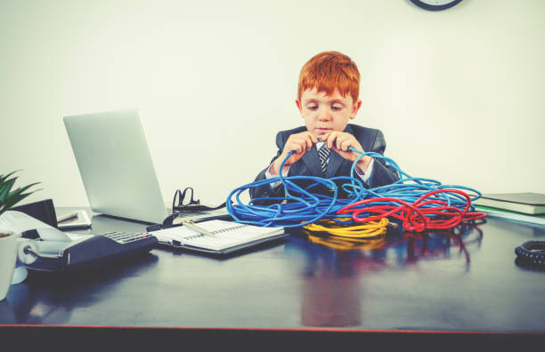 Humorous image of a child  IT professional working with a large pile of tangled internet cables on his desk. He is trying to reconnect his broken network.