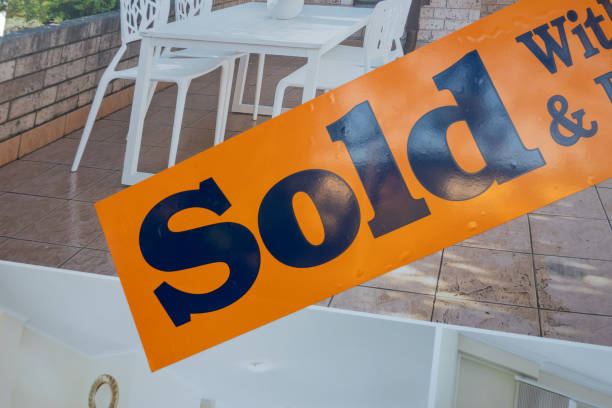 African American woman holding Sold sign in front of house