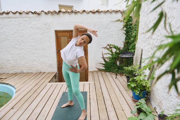 istock Woman practicing yoga outdoors on wooden deck surrounded by greenery, performing side stretch in peaceful setting 2175559426