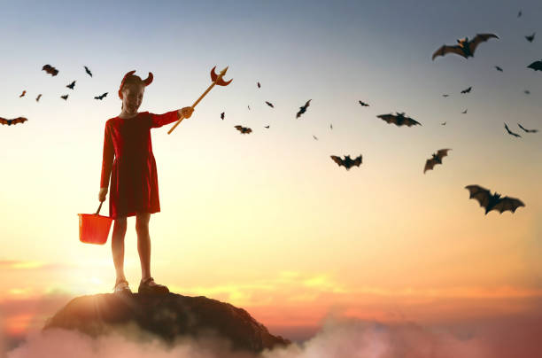 Happy little girl in devil costume at Halloween. Kid on moon sky background.