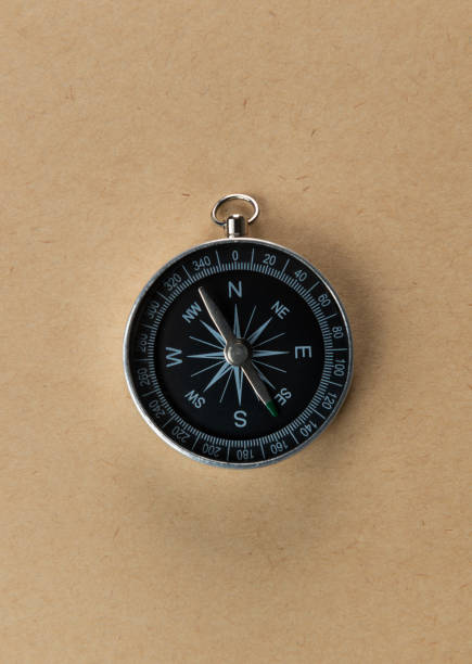 A close-up image of a classic black compass with silver edges placed on a plain beige background. This photo highlights the simplicity and functionality of the compass, making it ideal for themes of exploration, adventure, and decision-making.