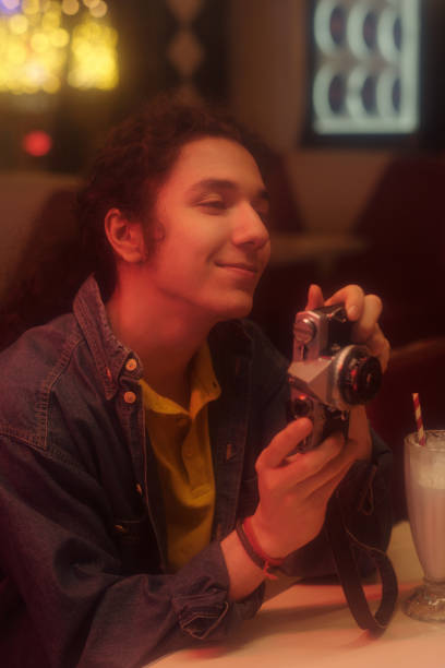 close up male hands holding retro camera and pressing shutter button on black shirt background