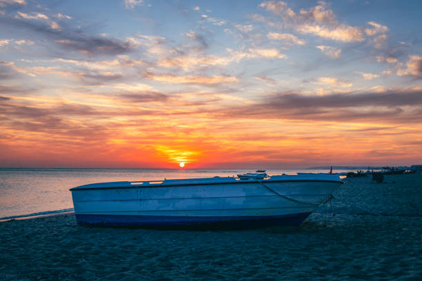 A small fisherman boat on beach at sunset time with blue and orange clouds