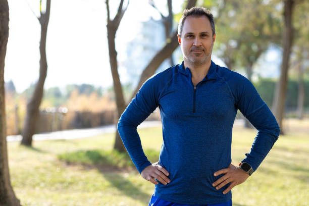Sportive adult man standing outside after a workout with contented emotion and his hands on his hips