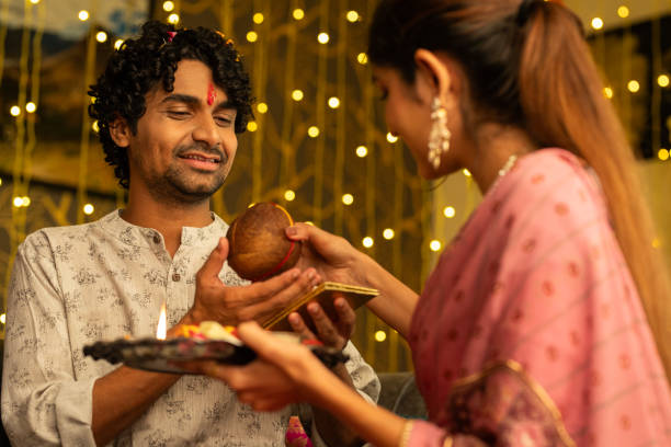 Sister giving religious offerings to brother during Bhai Dooj Sister giving coconut to smiling brother while celebrating Bhai Dooj festival in living room at home bhai tika stock pictures, royalty-free photos & images
