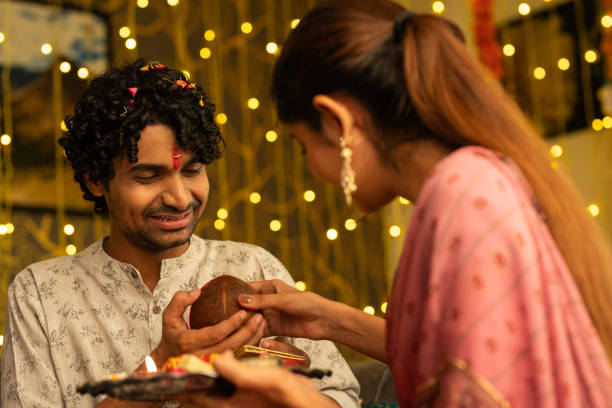 Sister giving religious offerings to brother during Bhai Dooj Sister giving coconut to smiling brother while celebrating Bhai Dooj festival in living room at home bhai tika stock pictures, royalty-free photos & images