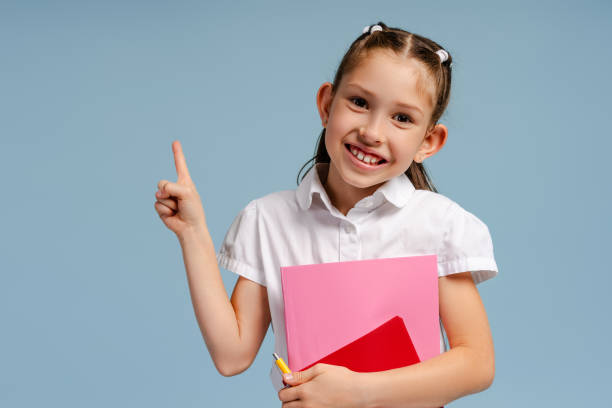 istock Smiling schoolgirl holding notebooks pointing up with finger 2175593399