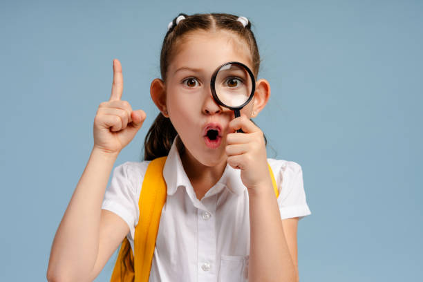 Surprised schoolgirl looking through magnifying glass having an idea
