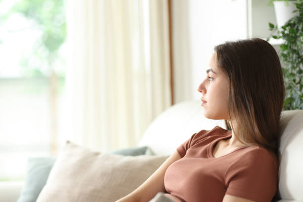 istock Serious woman looking through a window sitting at home 2175594862