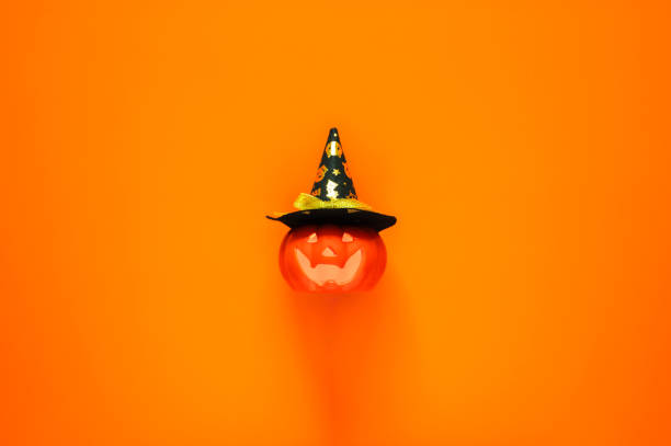 Halloween background with Jack o lantern that have light inside and wearing a hat on orange background. Minimal concept.