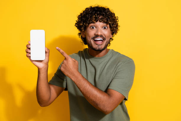 istock Photo of impressed guy dressed t-shirt indicating at menu on smartphone touchscreen empty space isolated on yellow color background 2175596400