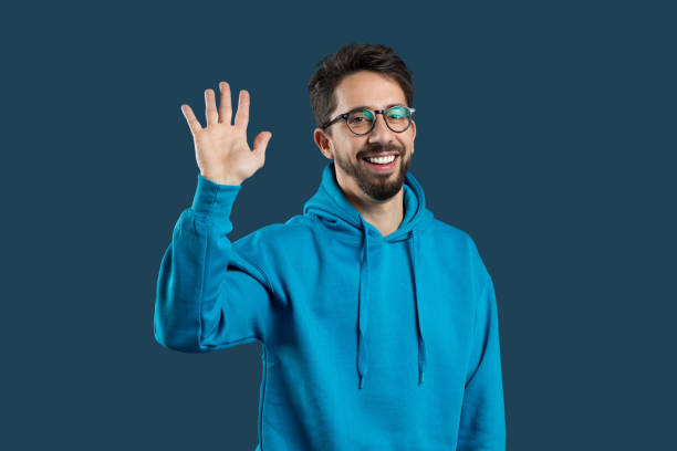 istock Smiling man waves while wearing a blue hoodie against a solid background 2175614818