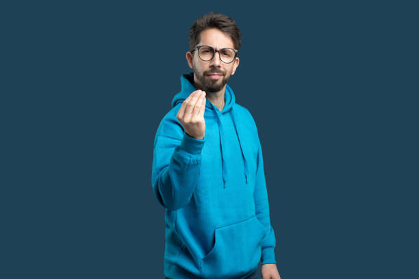istock Man in a blue hoodie gestures with his hand against a solid dark background 2175614830