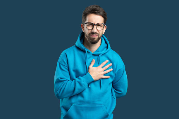Man in blue hoodie holding his chest against a solid background