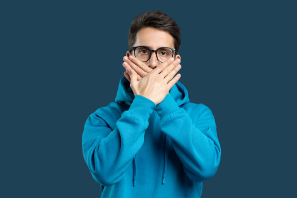 istock Young man in blue hoodie expressing silence with hands on face 2175614840