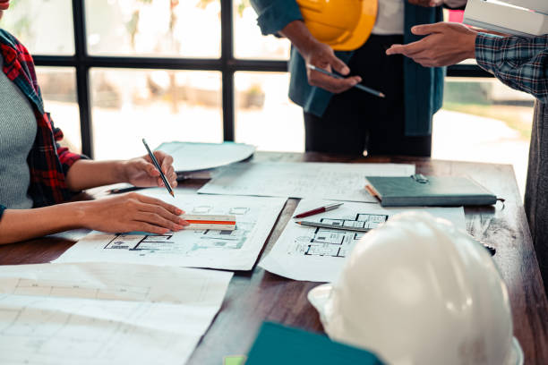istock Architects and engineers point to blueprints of architectural drawings inside a building to discuss construction plans, with hard hats and architectural documents scattered around. Close-up. 2175615273