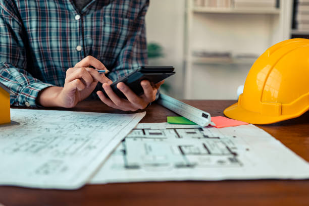 istock Architects and engineers point to blueprints of architectural drawings inside a building to discuss construction plans, with hard hats and architectural documents scattered around. Close-up. 2175615277
