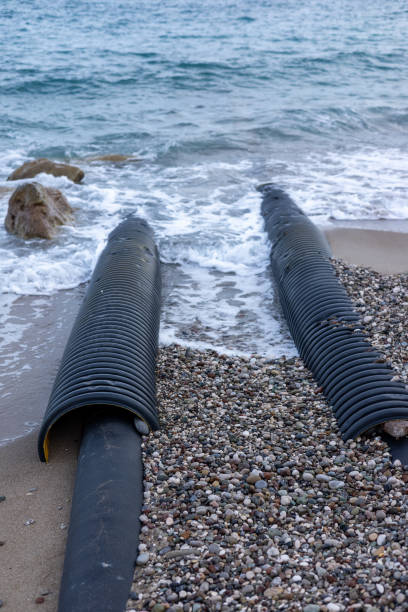 istock Black drainage pipes washed ashore on a rocky beach with gentle waves during daylight hours 2175617173