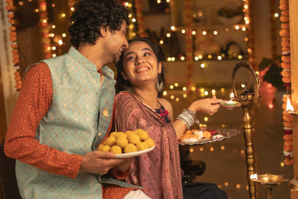 istock Young couple with diya and laddoos at home during Diwali celebration 2175620556