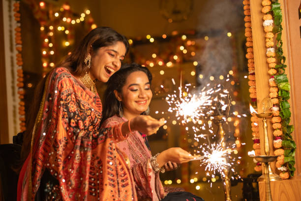 Female friends burning sparklers at home during Diwali celebration Cheerful beautiful sisters playing with sparklers while celebrating Diwali festival together at illuminated home india fireworks photos stock pictures, royalty-free photos & images