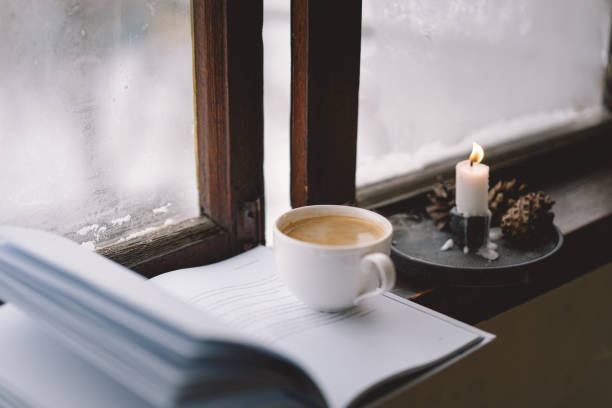 istock Cozy winter day with steaming coffee, open book, and candlelight by the snowy window 2175622921