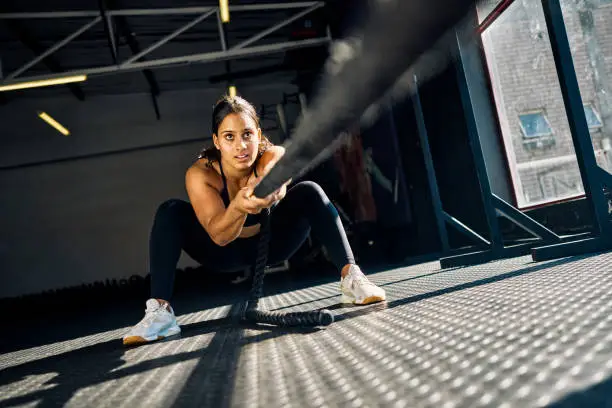 Female athlete pulling a weighted sled in a gym. Front view of a woman performing strength training exercise on a black gym floor. Hyrox Training Concept. Female athlete pulling a weighted sled in a gym. Front view of a woman performing strength training exercise on a black gym floor. Hyrox Training Concept.