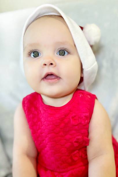 An adorable baby in red Christmas hat is smiling and sitting on the white background