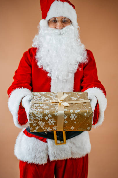 istock Santa Claus Holding A Gift Against A Beige Background 2175634660