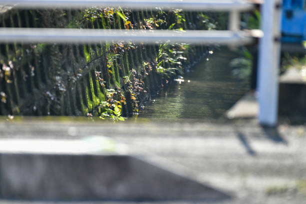 A stone wall of a small stream seen through the railings of the bridge.