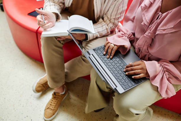 Black Woman Using Laptop Discussing with Colleague Work while Sitting In Office Center Cropped shot of unrecognizable African American woman typing on laptop keyboard discussing with male colleague business matters, while sitting on couch in lounge area of office center Lenovo Yoga 9i students laptops stock pictures, royalty-free photos & images