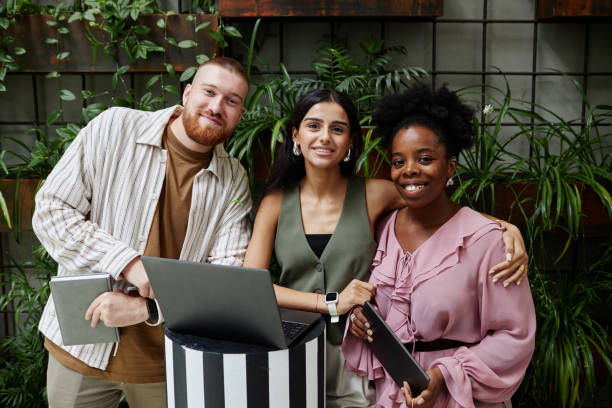 istock Creative Team of Thee Smiling Businesspeople Using Digital Devices in Cafe with Plants 2175655043