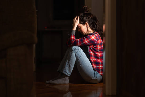 istock Panic disorder and obsessive-compulsive disorder. Suffering young Caucasian woman sits down on floor in despair in dark living room. Concept of psychology and mental problems 2175655225