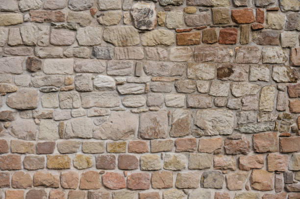 A detailed view of a stone masonry wall made of variously sized and shaped stones. The warm, earthy tones of the stones create a rustic and sturdy appearance, showcasing traditional construction techniques.