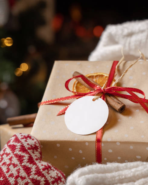 istock Round gift tag on a Christmas present near white sweater against Christmas tree lights, mockup 2175659876