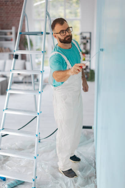 istock Painter in overalls painting blue wall with roller tool 2175663958