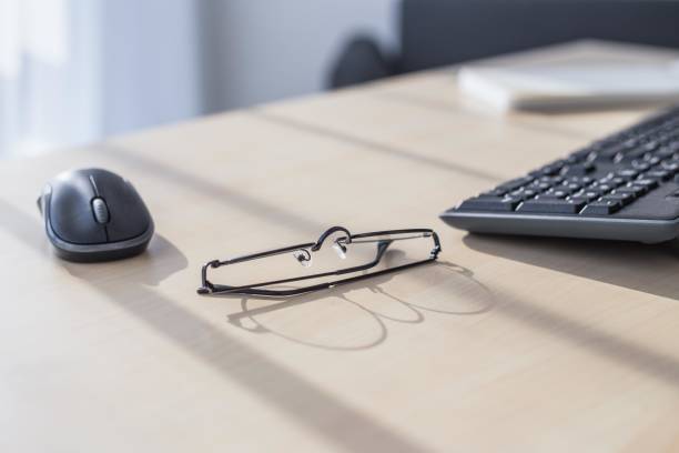 Black framed glasses on an office desk with a keyboard and mouse