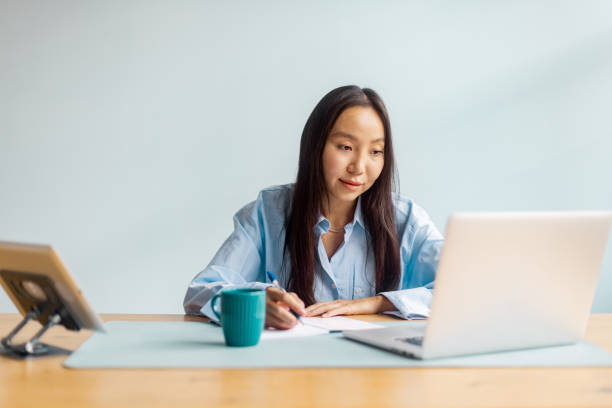 istock Woman in blue shirt writes notes beside her laptop. 2175666303