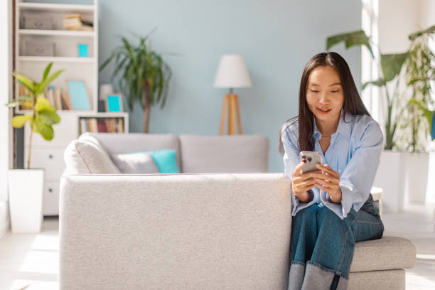 istock Woman sitting on couch using smartphone in living room 2175669990