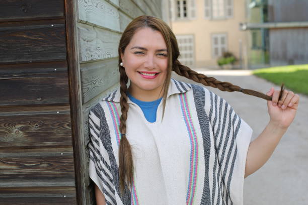 A Hispanic woman in her thirties is walking around in a village. She wears a traditional Colombian poncho called 
