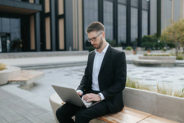 istock Focused Professional in Suit Using Laptop Outdoors by Modern Office Building 2175686563