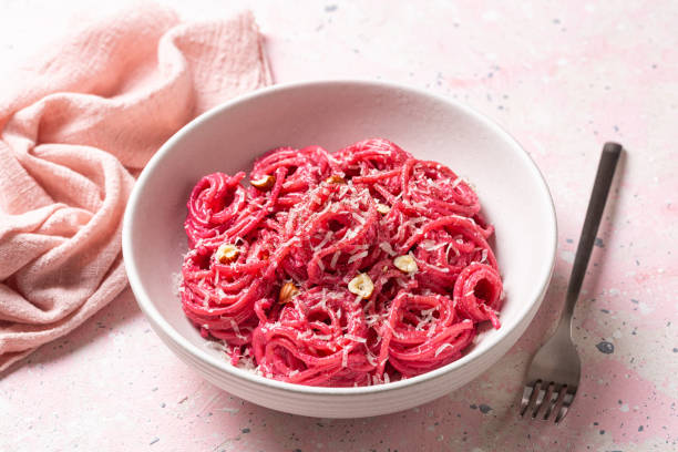 Creamy Beet Pasta spaghetti with hard cheese, nuts and black pepper. Close up, pink background.